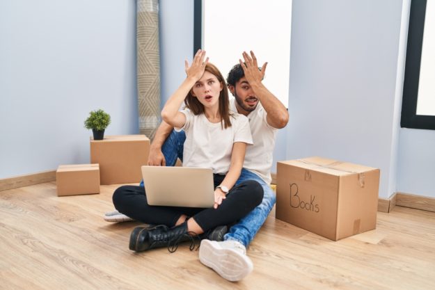 Young,Couple,Using,Laptop,At,New,Home,Surprised,With,Hand
